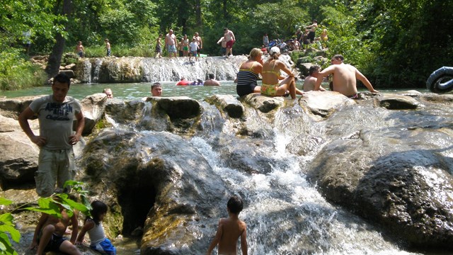 a swimming hole and waterfall with dozens of people