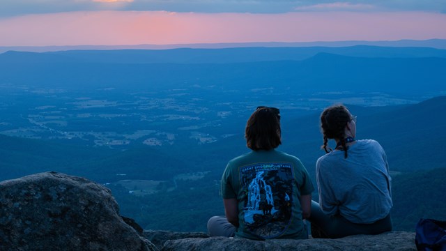 Two hikers watch the sunset from a summit